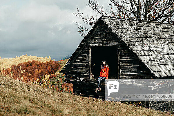 Happy young girl sitting on a barn in the mountains during autumn