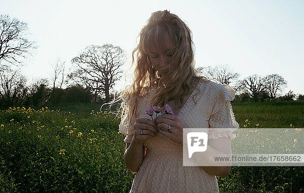 blonde curly haired woman holding flowers in a field at sunset