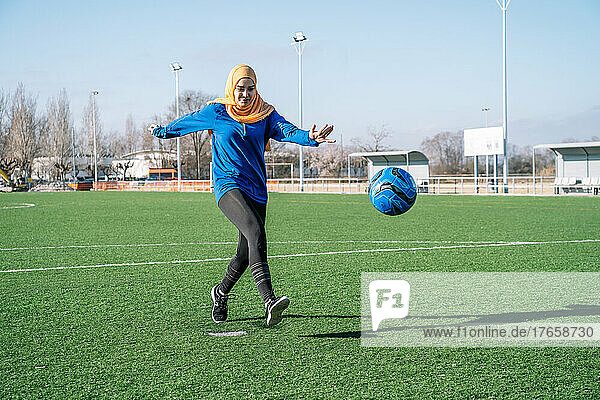 Ethnic woman playing football on sports field in stadium