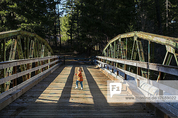 A young girl runs across old wooden bridge in sunshine