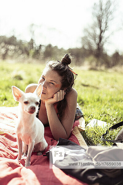 beautiful woman with small chihuahua lays in sun on grass in nature
