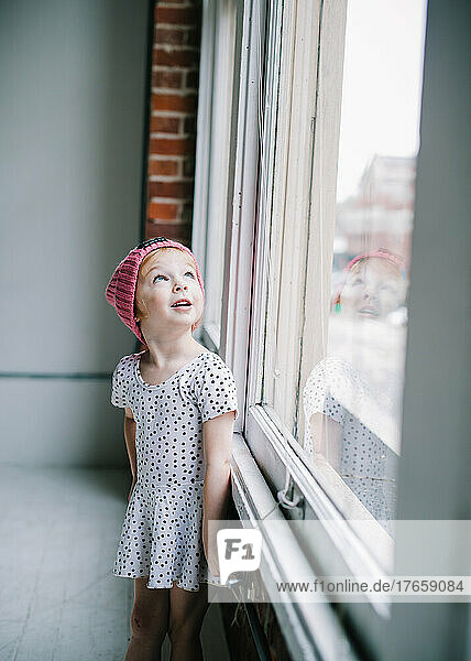 toddler girl in polka dot dress looking out window behind her