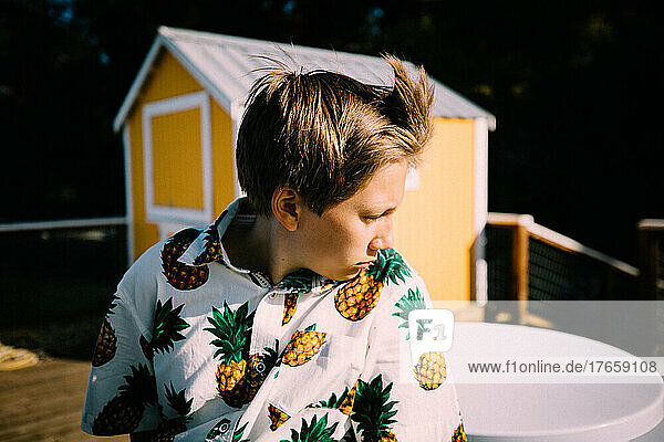 Teen Boy in Pineapple Shirt Looks Towards the Sunset on Windy Dock
