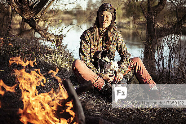 mixed race person in afternoon sun by water and fire with small dogs