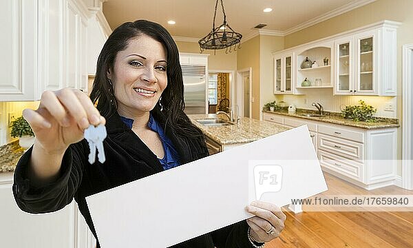Hübsche hispanische Frau in der Küche mit Hausschlüssel und weißem Schild