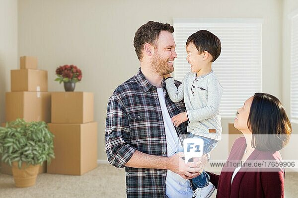 Young mixed-race caucasian and chinese family inside empty room with moving boxes