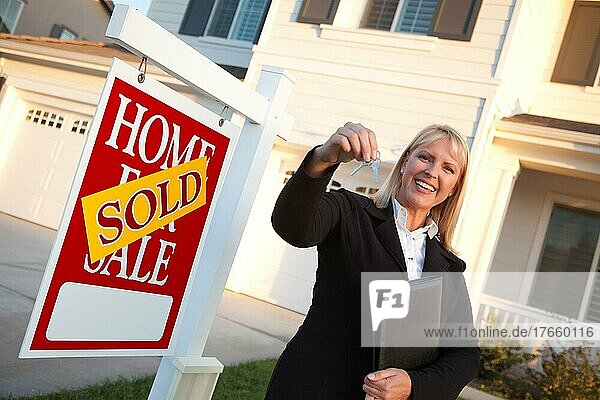 Weiblicher Immobilienmakler bei der Übergabe der Hausschlüssel vor einem schönen neuen Haus und einem Immobilienschild
