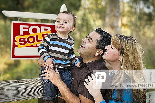 Glückliches gemischtrassiges Paar mit Baby vor einem Schild mit verkauften Immobilien