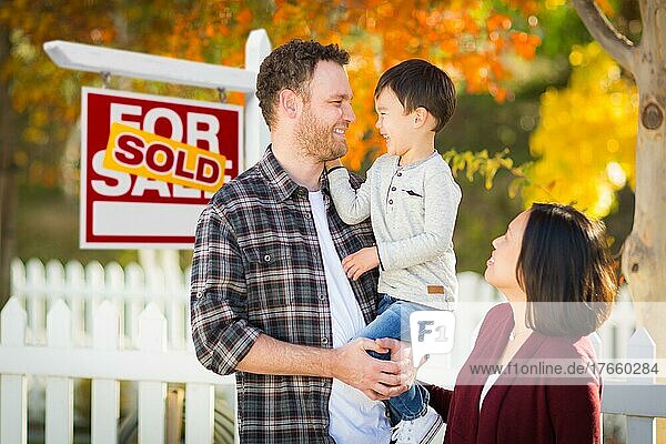Gemischtrassige chinesische und kaukasische Eltern und Kind vor einem Zaun und einem zum Verkauf stehenden Immobilienschild