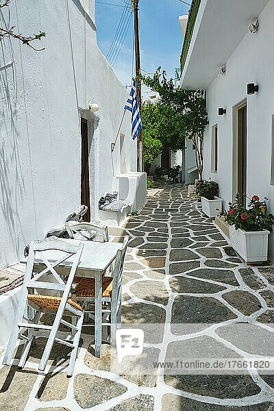 Picturesque narrow street with traditional whitewashed houses with greek flag and cafe tables in Naousa town in famous tourist attraction Paros island  Greece
