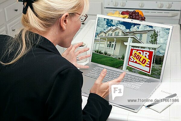 Aufgeregte Frau in der Küche  die einen Laptop benutzt  um ein Haus zu verkaufen oder zu kaufen. Der Bildschirm kann leicht für Ihre eigene Nachricht oder ein Bild verwendet werden