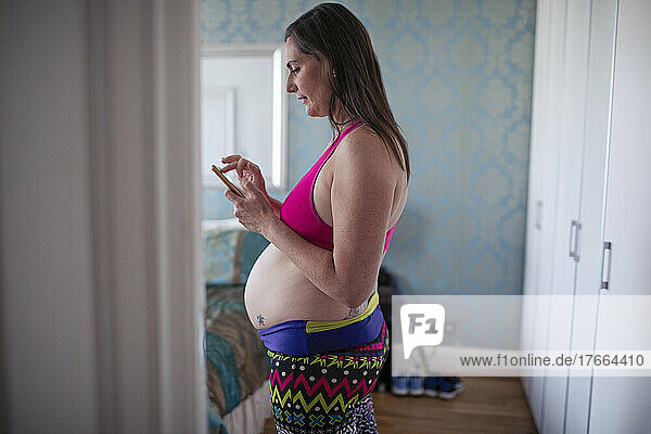 Schwangere Frau im Sport-BH benutzt ihr Smartphone in der Haustür