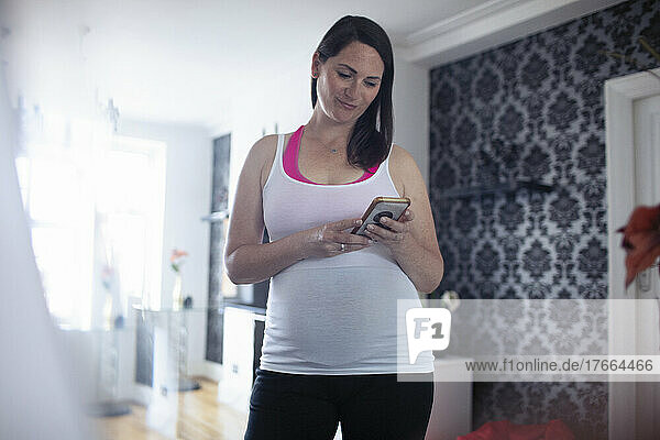Schwangere Frau in Tanktop mit Smartphone