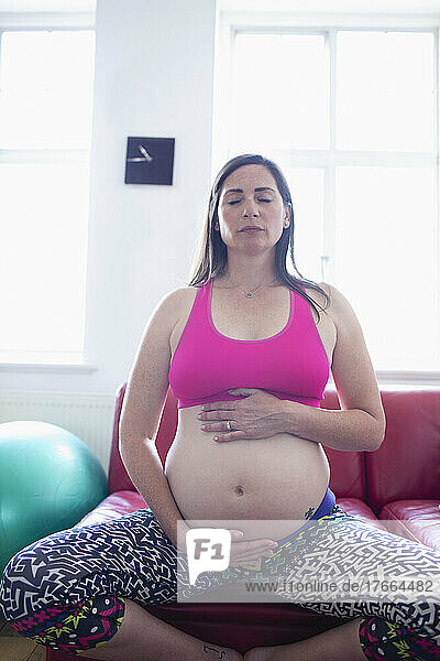 Serene schwangere Frau meditiert und hält Babybauch