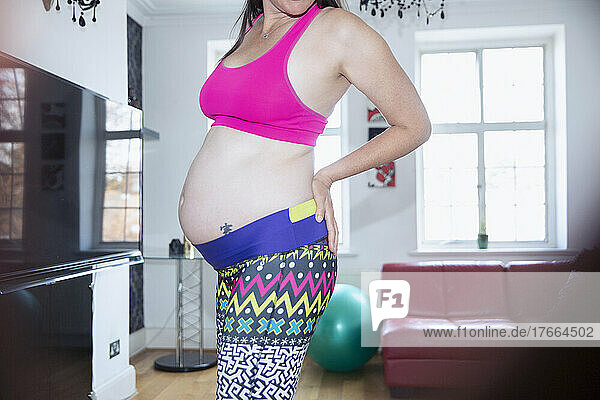 Schwangere Frau in Sport-BH und Leggings beim Training zu Hause