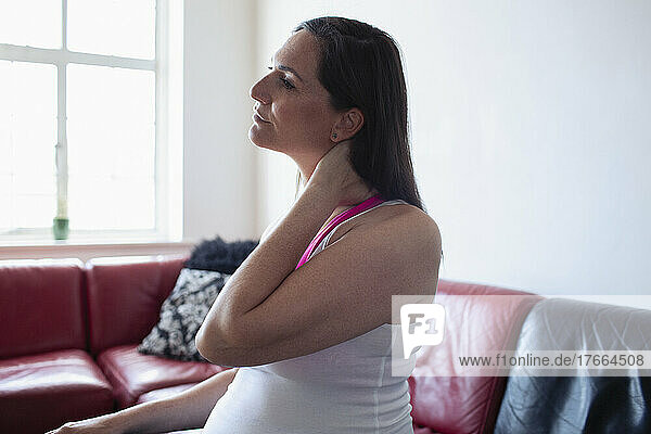 Pregnant woman rubbing neck on sofa