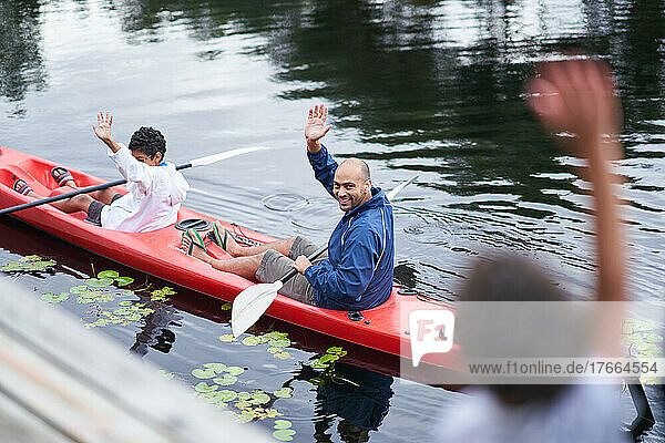 Glücklicher Vater und Sohn winken vom Kajak aus auf dem Fluss