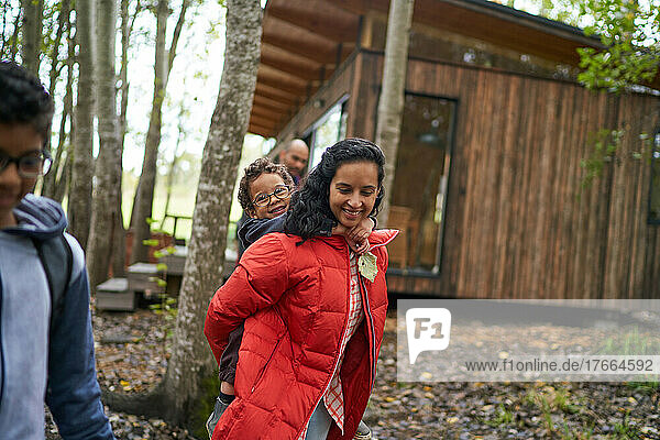 Portrait mother piggybacking outside cabin in woods