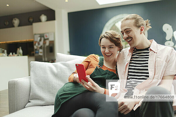 Happy young couple with smart phone on living room sofa
