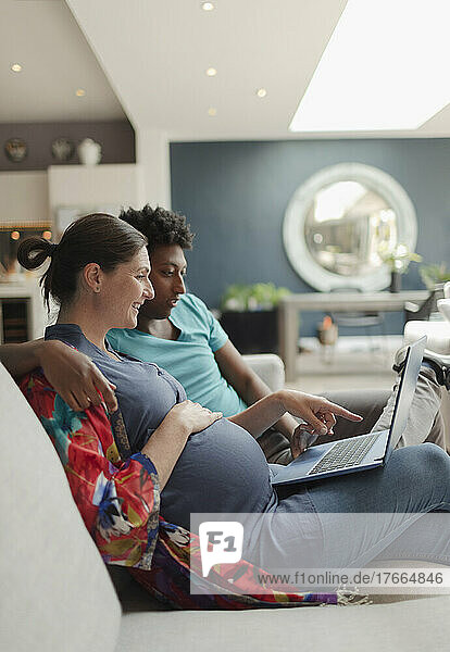 Schwangeres Paar mit Laptop auf dem Wohnzimmersofa
