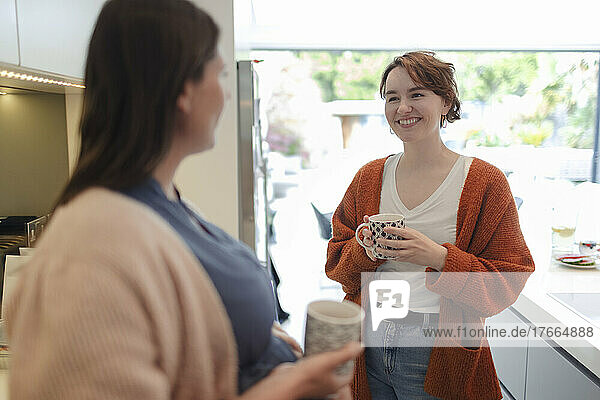 Young women friends talking and drinking coffee in kitchen
