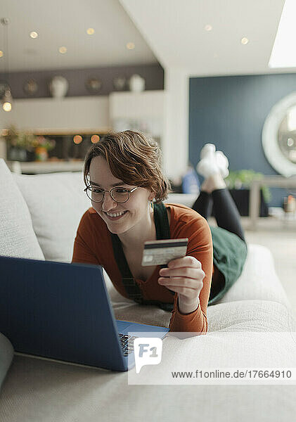 Glückliche junge Frau mit Kreditkarte beim Online-Shopping am Laptop auf dem Sofa