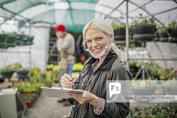 Portrait happy female garden shop owner with clipboard in greenhouse