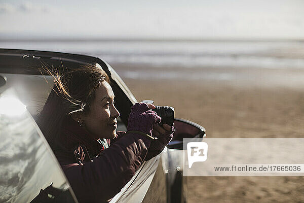 Frau mit Digitalkamera im Cabrio am Strand