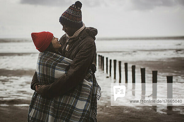 Glückliches Paar in Decke eingewickelt am Winterstrand