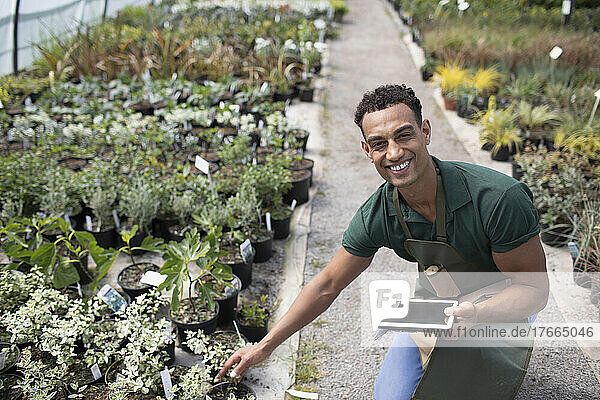 Portrait happy male garden shop owner with digital tablet and plants