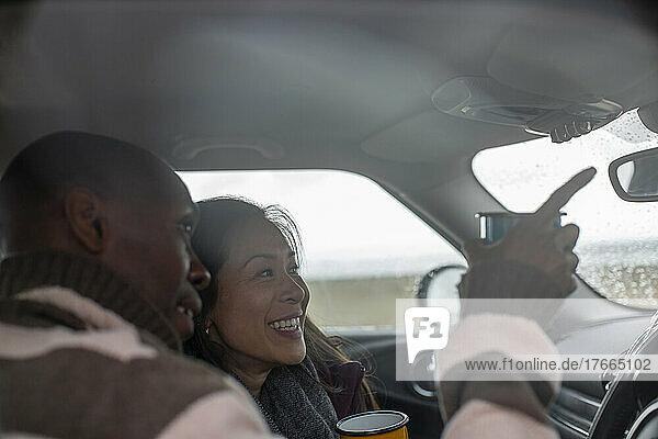 Happy couple with coffee on road trip in car