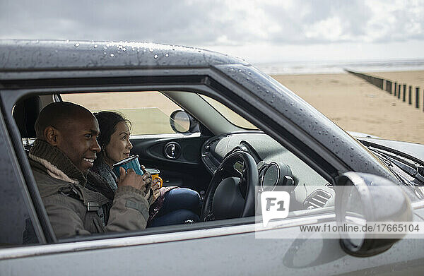 Glückliches Paar trinkt Tee im Auto am nassen Winterstrand