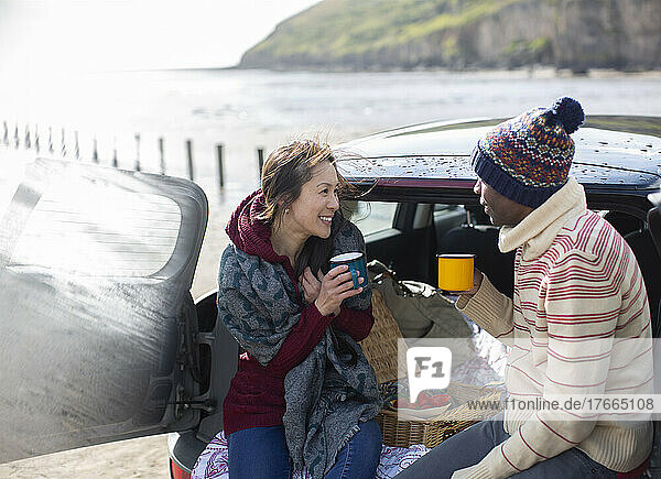 Happy couple drinking coffee at back of car on beach