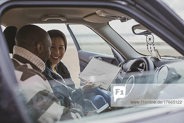 Glückliches Paar auf Autoreise mit Skizzenblock im Auto