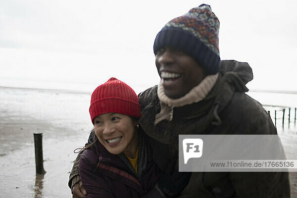 Happy affectionate couple in warm clothing hugging on winter beach
