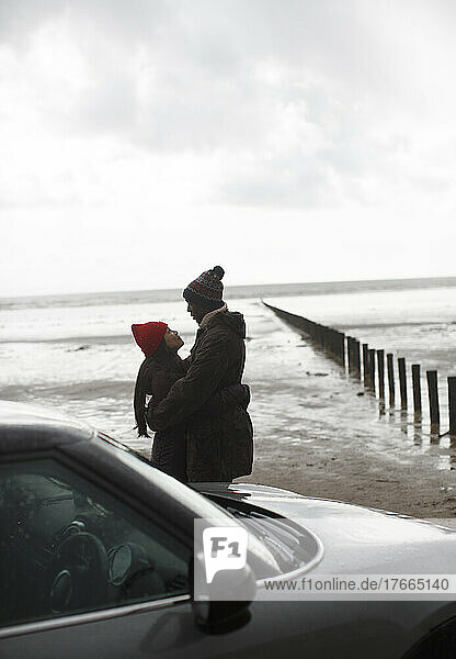 Zärtliches Paar in warmer Kleidung  das sich am nassen Winterstrand umarmt