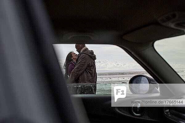 Zärtliches Paar  das sich außerhalb des Autos am Strand umarmt