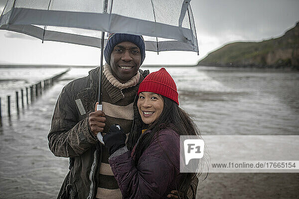 Portrait happy couple under umbrella on wet winter beach