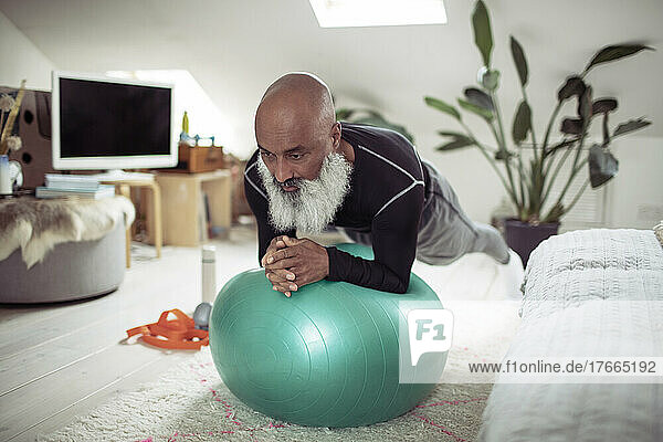Mature man with beard exercising with fitness ball at home