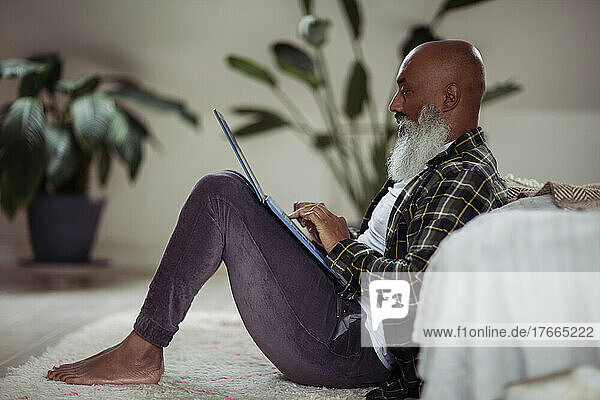 Älterer Mann mit Bart benutzt Laptop auf dem Boden