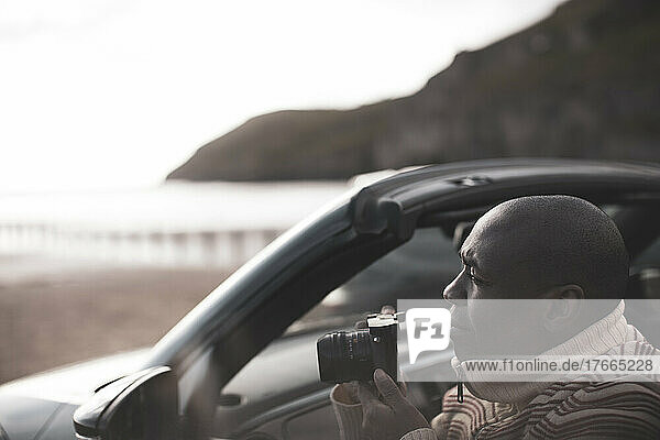 Mann mit Digitalkamera im Cabrio am Strand
