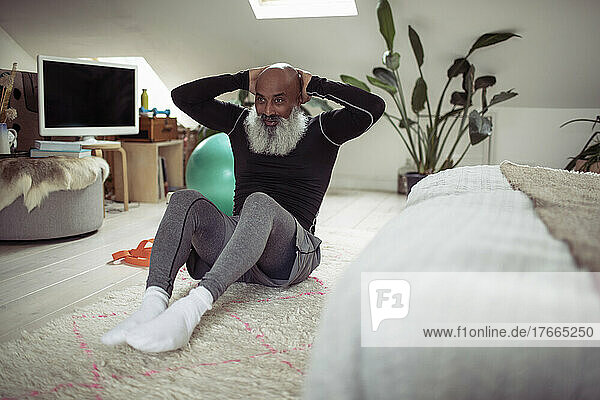 Älterer Mann mit Bart macht Sit-ups auf dem Schlafzimmerboden