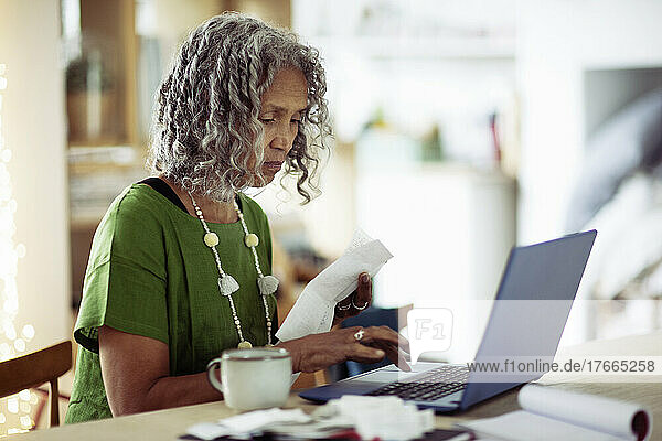 Senior woman with receipts banking at laptop