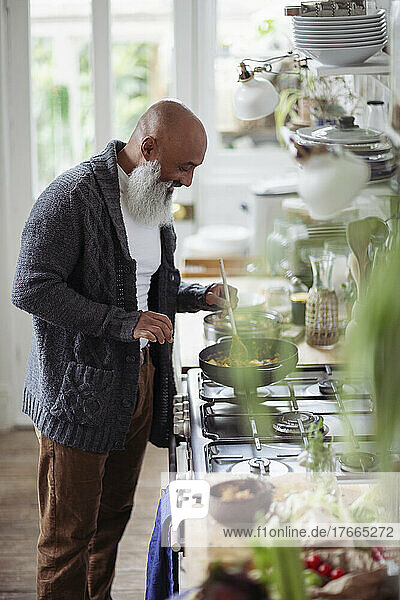 Senior man with beard cooking at kitchen stove