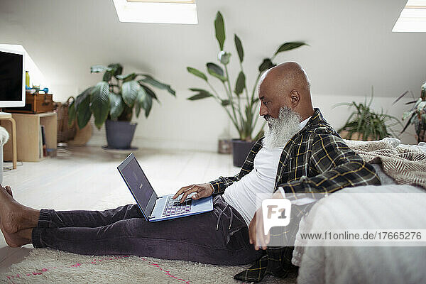 Mature man with beard using laptop on bedroom floor