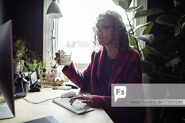 Ältere Frau mit Tee bei der Arbeit am Computer im Heimbüro