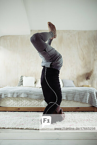 Mann übt Yoga-Kopfstand-Pose auf Schlafzimmerteppich