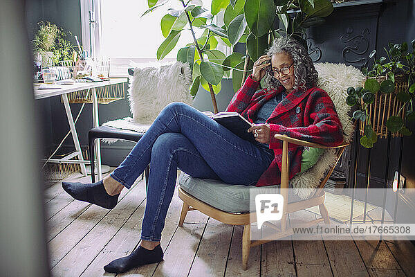 Ältere Frau liest ein Buch im Sessel zu Hause