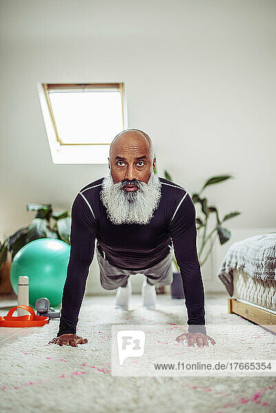 Konzentrierter reifer Mann  der in Plankenhaltung auf dem Schlafzimmerboden trainiert