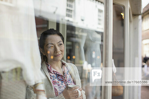 Female shop owner drinking tea at shop window